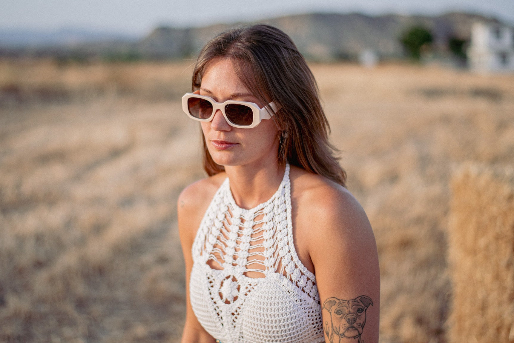 Woman wearing sunglasses and a white crochet top in a desert-like setting