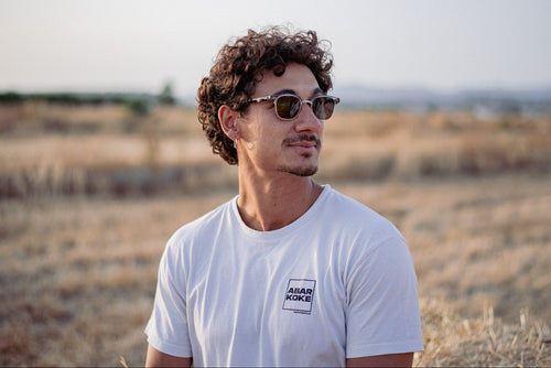 Man wearing sunglasses and a white t-shirt with a logo in an open field